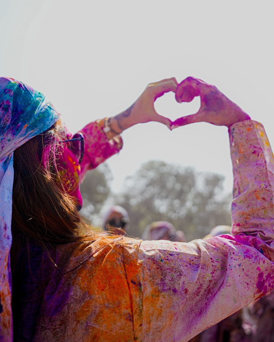 Viajera de espaldas formando un corazón con las manos, con la ropa cubierta de polvo de colores durante Holi