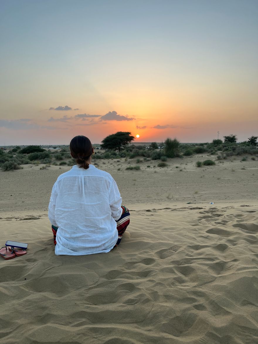 Viajera sentada en la arena del desierto del Thar mirando la puesta de sol