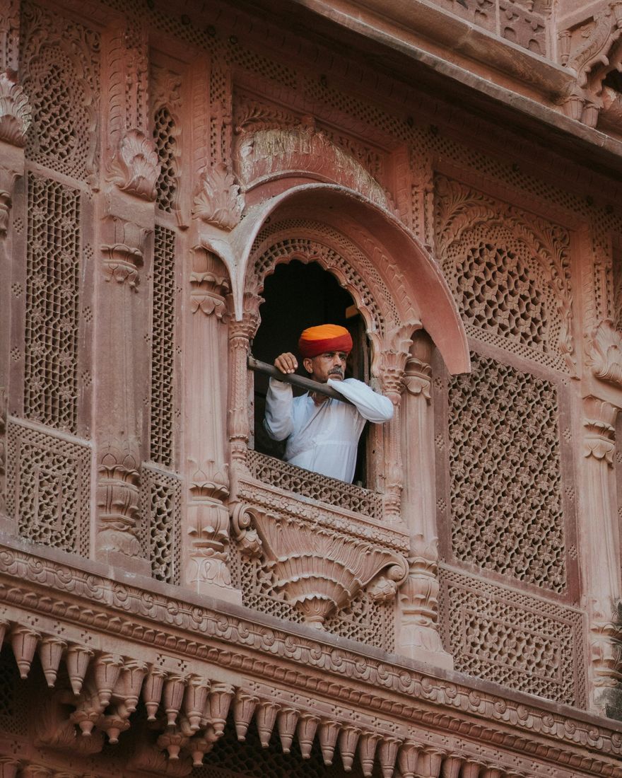 Hombre con turbante naranja asomado a un balcón de arenisca tallada del fuerte de Mehrangarh