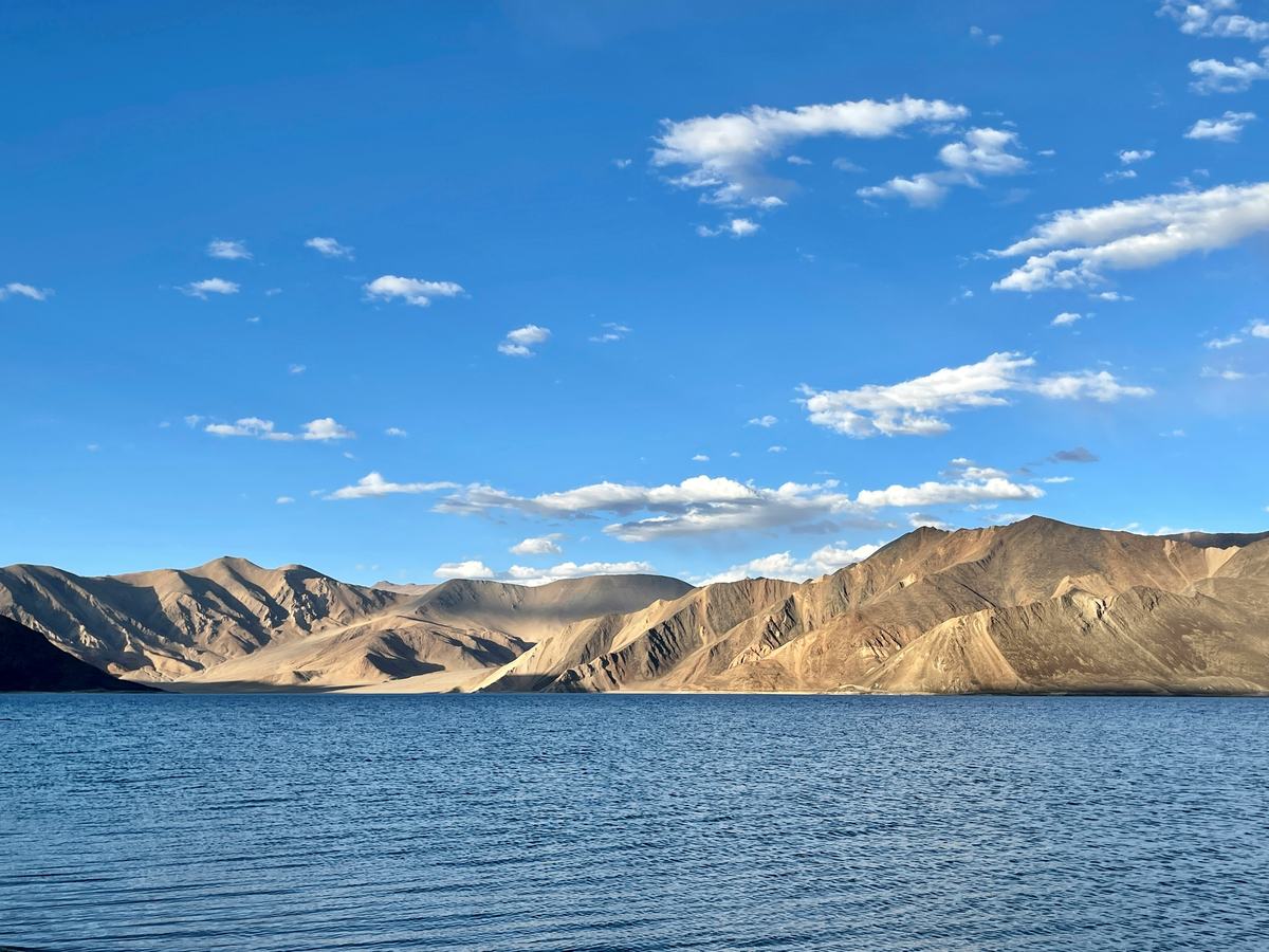 Lago Pangong de color azul intenso con montañas ocres y nubes blancas al fondo, en Ladakh