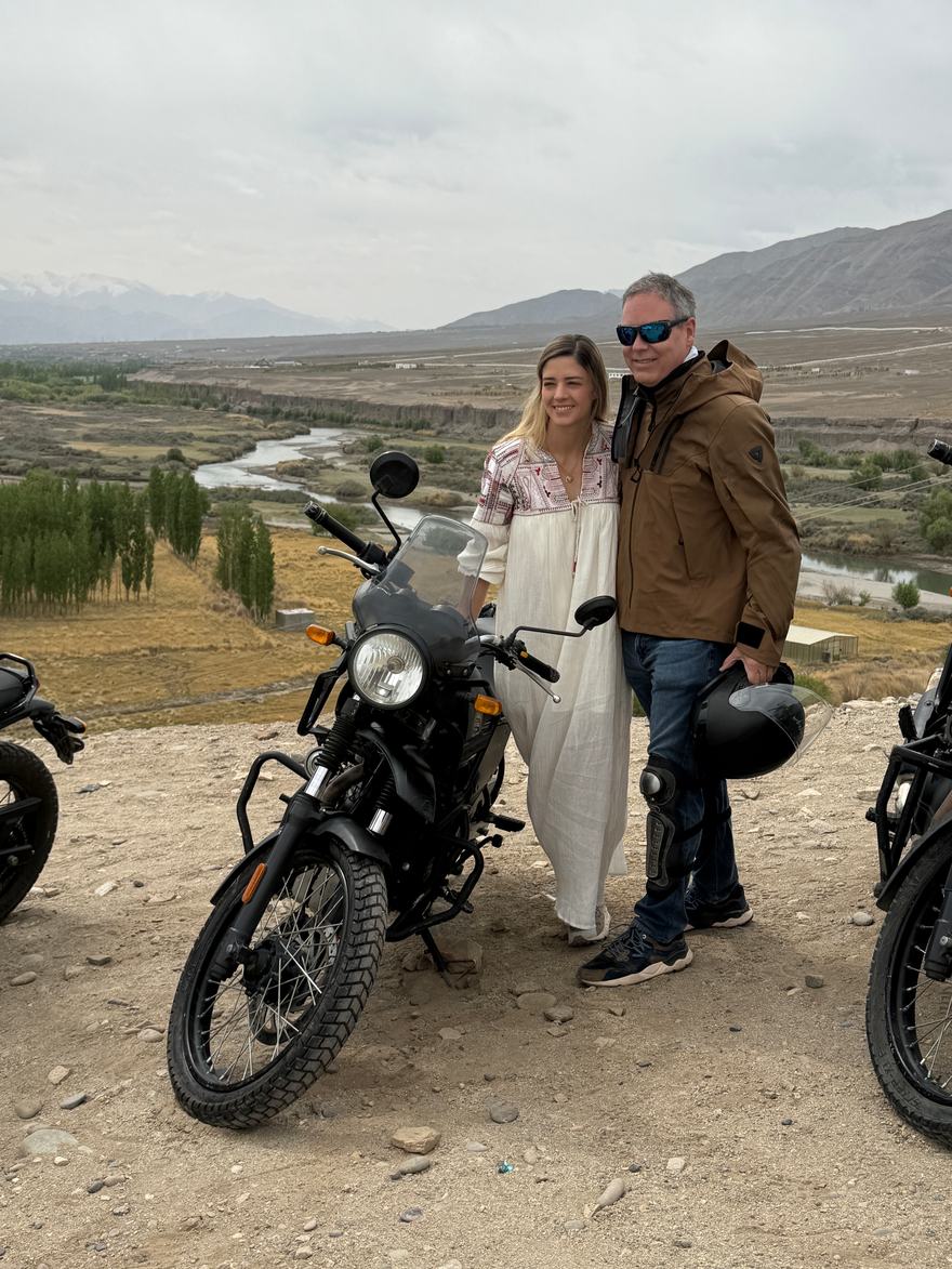 Pareja de viajeros junto a una Royal Enfield Himalayan sobre el valle del río Indo, cerca de Leh