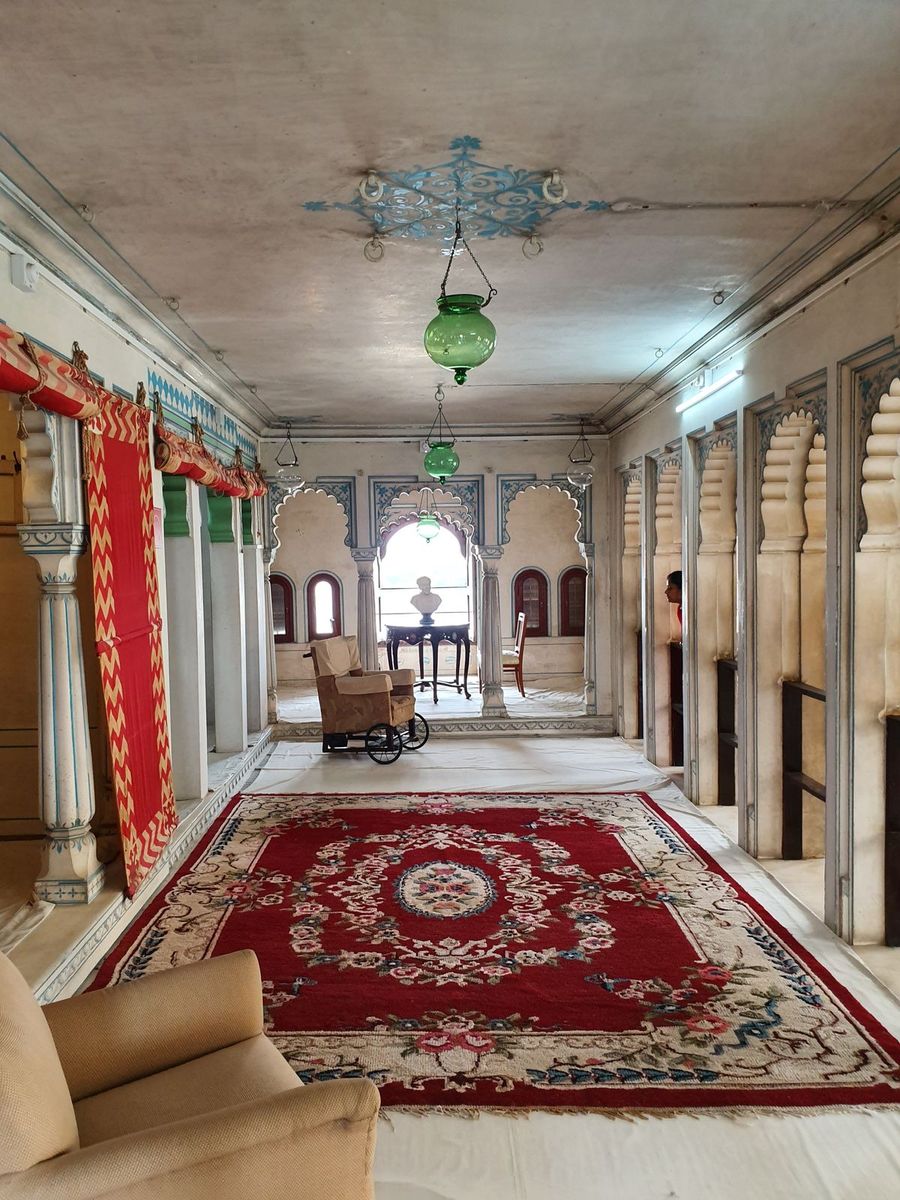 Galería interior del Palacio de la Ciudad de Udaipur, con alfombra roja, lámpara de cristal y arcos de piedra