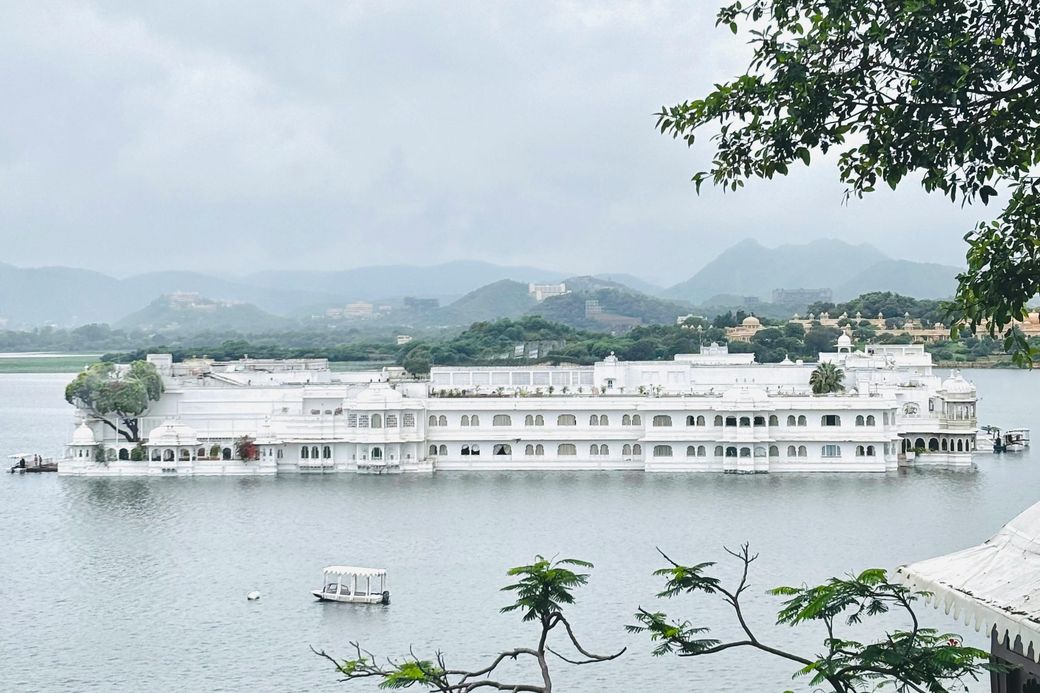 El Taj Lake Palace, blanco sobre el lago Pichola, con colinas verdes al fondo