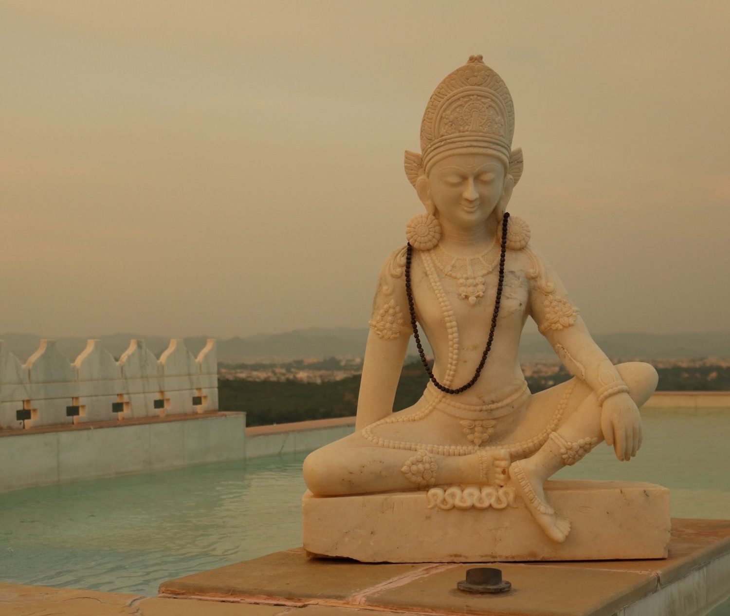 Escultura de piedra junto a una terraza con piscina, al atardecer, en la India