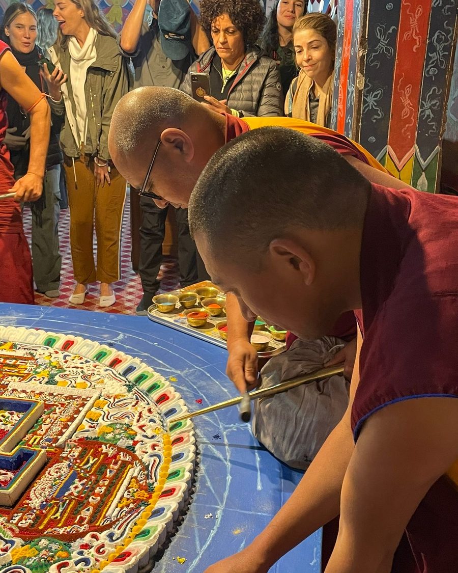 Monjes budistas construyen un mandala de arena mientras un grupo de viajeros lo observa