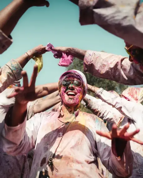 Un hombre cubierto de color celebra Holi con los brazos en alto