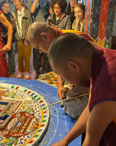Monjes budistas construyen un mandala de arena mientras un grupo de viajeros lo observa