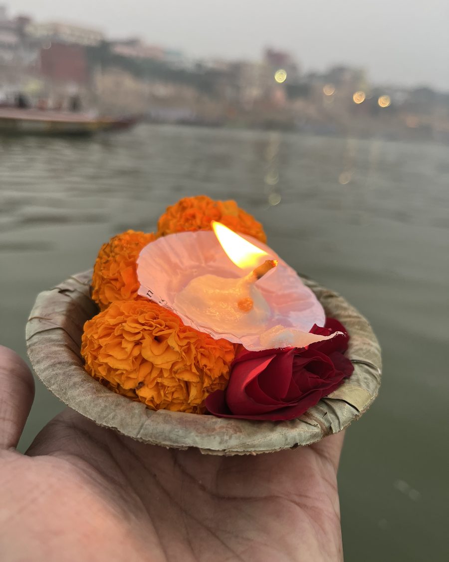 Una mano sostiene una lámpara de aceite entre pétalos de caléndula antes de ofrecerla al Ganges, en Varanasi