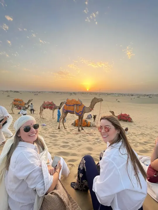 Dos viajeras contemplan la puesta de sol junto a los camellos en el desierto de Rajastán