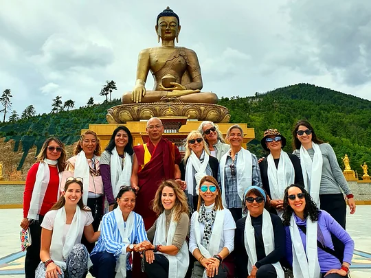 Grupo de viajeras con chalinas blancas posa con un monje budista ante la gran estatua dorada del Buda Dordenma, en Bután