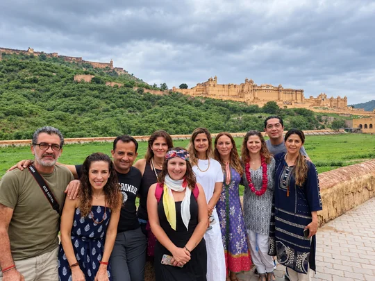 Un grupo de viajeros sonríe ante el Fuerte Amber y las murallas sobre la colina verde, en Jaipur
