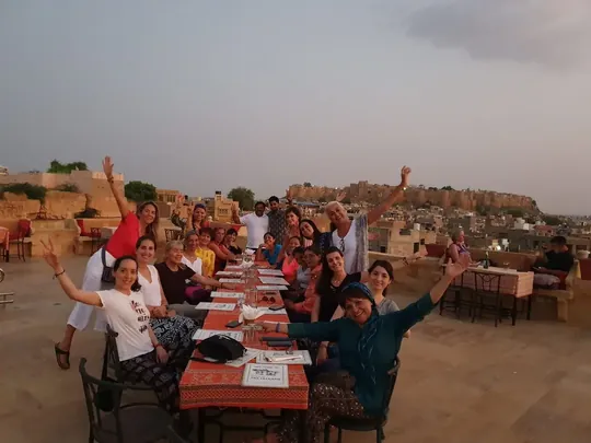 Grupo de viajeros en una comida en una larga mesa de azotea, con la ciudad dorada de Jaisalmer al fondo