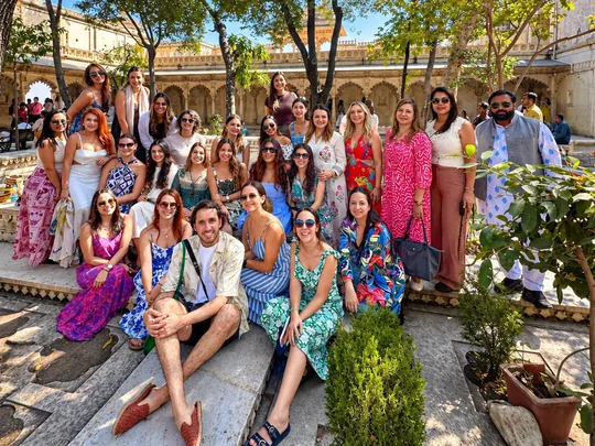 Un grupo numeroso de viajeros con ropa de colores posa a la sombra de los árboles en un patio del City Palace de Udaipur