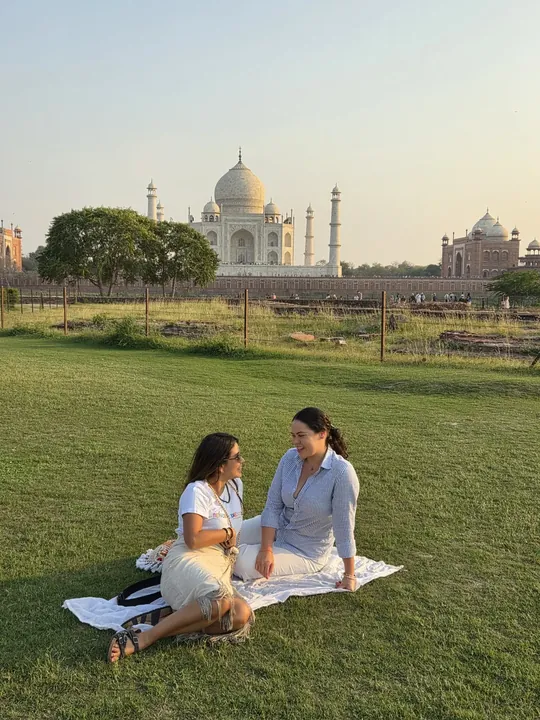 Dos viajeras sentadas sobre el césped con el Taj Mahal al fondo, al atardecer