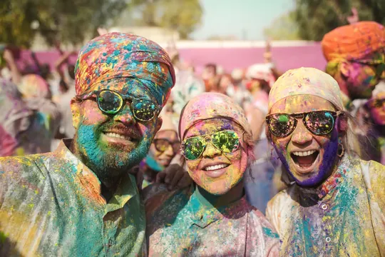 Viajeros con el rostro cubierto de pigmento sonríen durante el festival Holi
