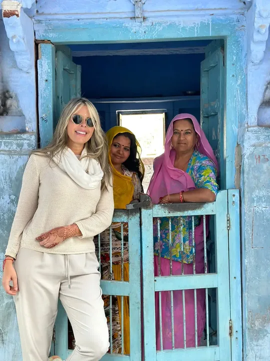 Una viajera junto a dos mujeres locales en la puerta azul de una casa en Rajastán